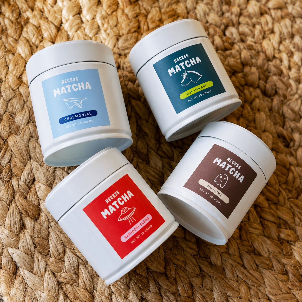 Four containers of matcha on a woven surface