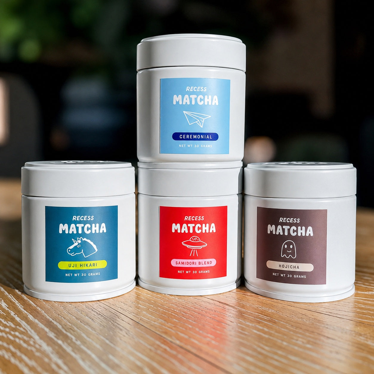 Four containers of Recess Matcha on a wooden surface with colorful labels.
