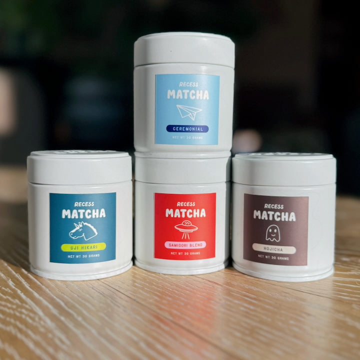Four containers of Recess Matcha on a wooden surface with colorful labels.